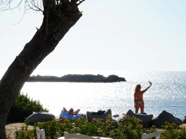 Woman taking a selfie in front of the glittering sea at Olive Tree Beach in Pegeia