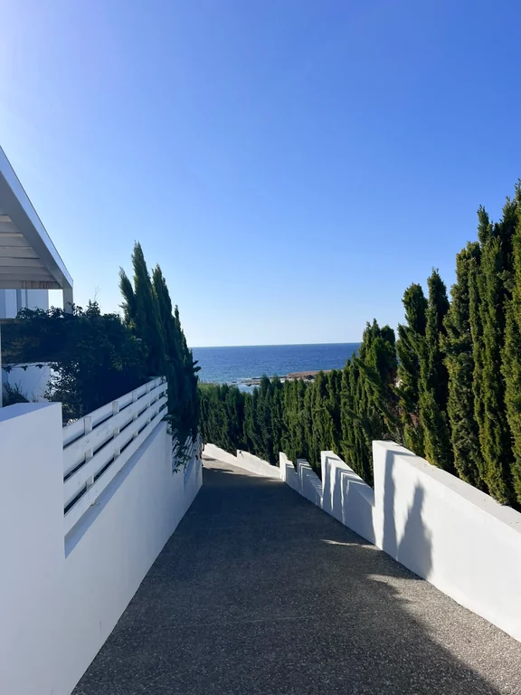 Path between white walls and cypress trees leading to Olive Tree Beach at Cap St Georges
